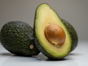 Eine halbierte Avocado mit Kern, die vor zwei ganzen Avocados lehnt.