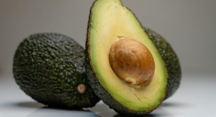 Eine halbierte Avocado mit Kern, die vor zwei ganzen Avocados lehnt.
