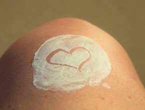 Ein menschliches Knie mit weißer Creme darauf, in die ein Herz gemalt ist.