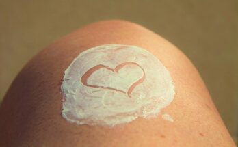 Ein menschliches Knie mit weißer Creme darauf, in die ein Herz gemalt ist.
