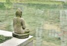 Eine steinerne Buddha-Figur an einem Teich.