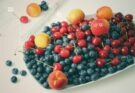 Fruchtfliegen auf einer Schale Obst mit Blaubeeren, Kirschen, Aprikosen