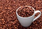 Eine weiße Tasse gefüllt mit Kaffeebohnen, die inmitten von Kaffeebohnen steht.