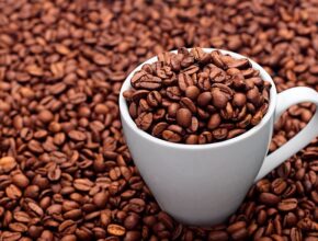 Eine weiße Tasse gefüllt mit Kaffeebohnen, die inmitten von Kaffeebohnen steht.