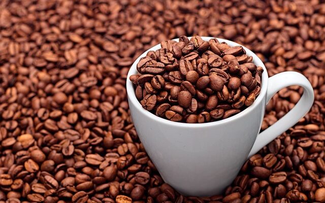 Eine weiße Tasse gefüllt mit Kaffeebohnen, die inmitten von Kaffeebohnen steht.