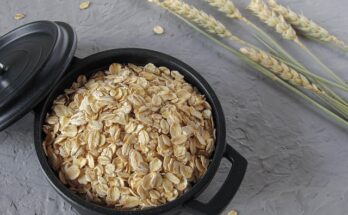 Ein kleiner Topf mit Haferflocken, daneben ein paar Haferhalme.