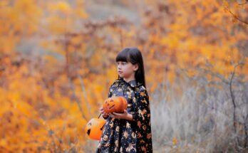 Ein junges Mädchen mit dunklen langen Haaren in einer Halloweenverkleidung und mit zwei Kürbissen in den Händen.