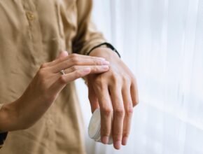 Jemand, der sich seine Hände mit einer Creme eincremt; in der einen Hand den Tiegel.